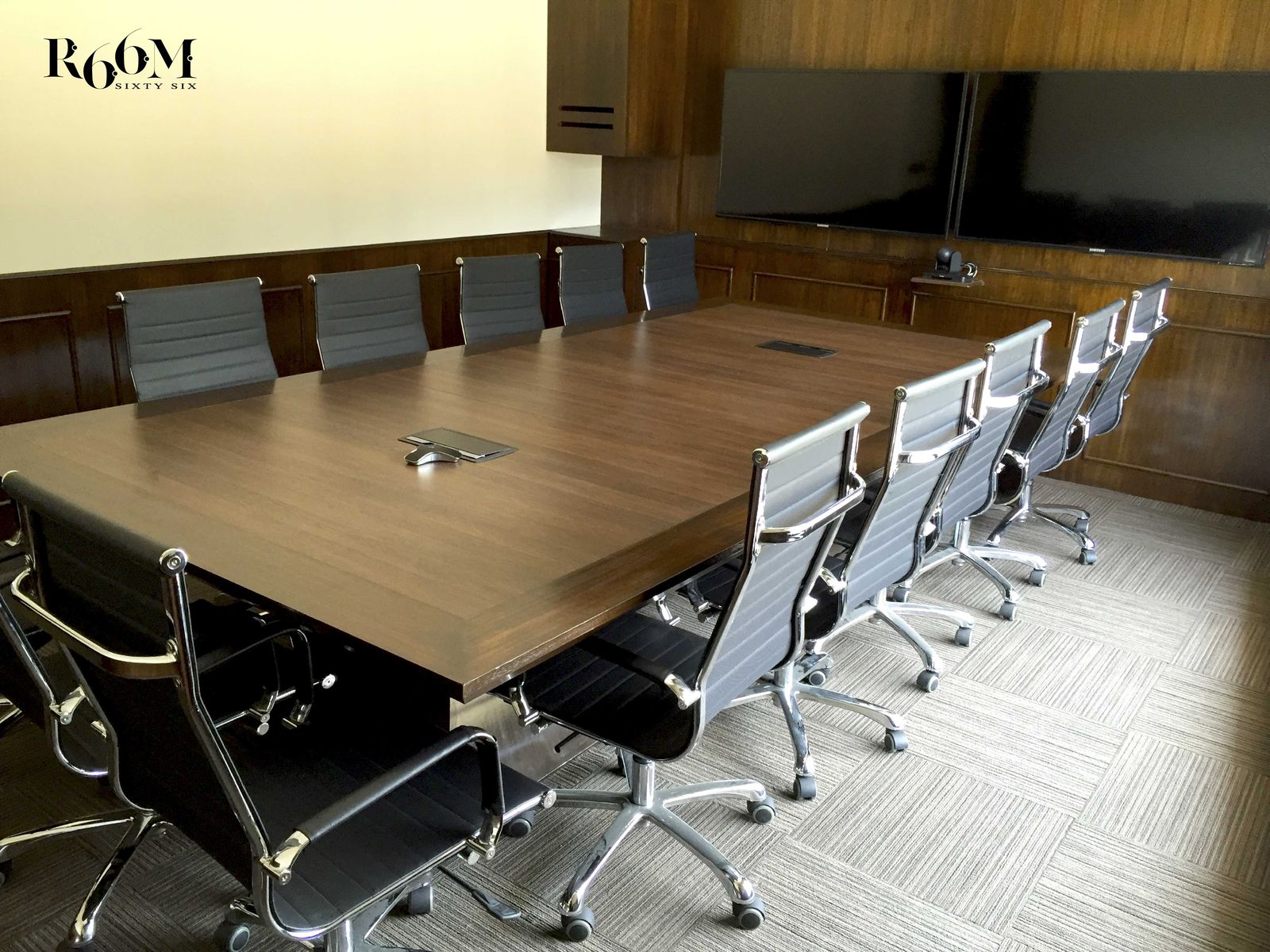 Conference room with a long walnut table, black chairs and two wall screens